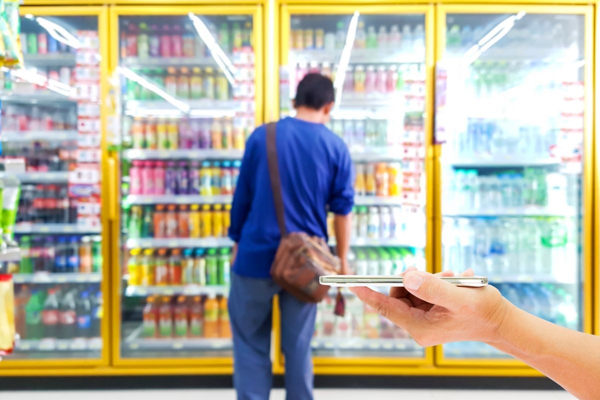 use mobile phone, blur image of laborer aMan re looking for the drinks they need in beverage cooler.